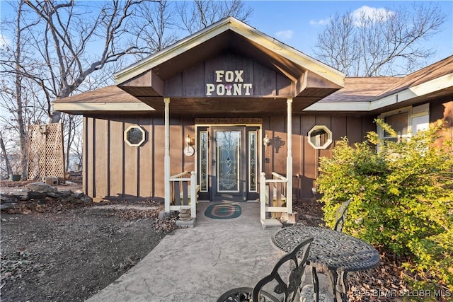 doorway to property with board and batten siding and a shingled roof