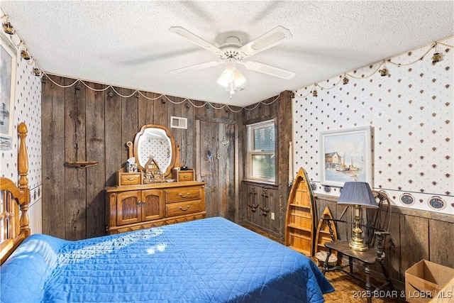 bedroom featuring a textured ceiling, a ceiling fan, visible vents, wood walls, and wainscoting