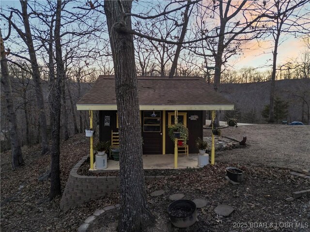 back of house at dusk with a patio area and a shingled roof