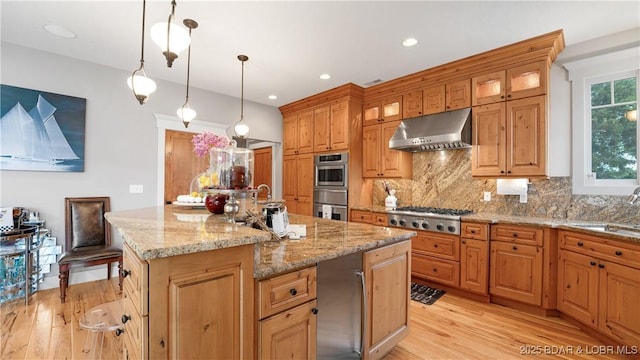 kitchen featuring an island with sink, stainless steel appliances, light wood-style floors, under cabinet range hood, and backsplash