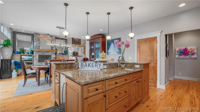 kitchen featuring dark stone countertops, an island with sink, light wood-type flooring, and a sink