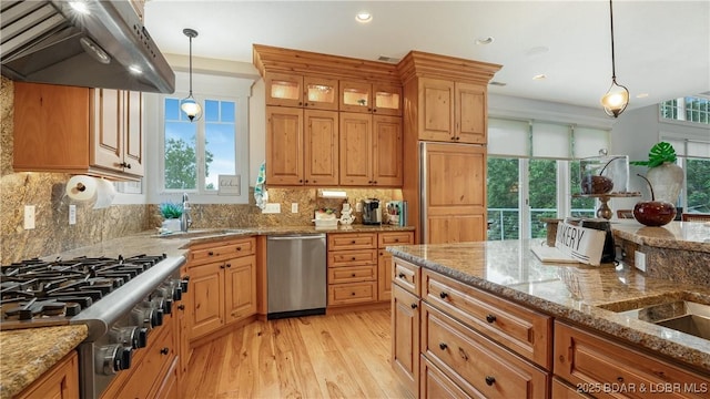 kitchen with under cabinet range hood, a sink, tasteful backsplash, appliances with stainless steel finishes, and light wood finished floors