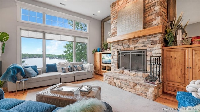 living area featuring a towering ceiling, a fireplace, visible vents, and light wood finished floors