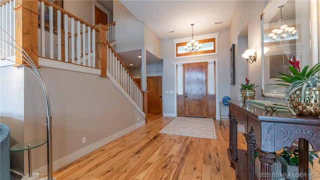 entryway with hardwood / wood-style flooring, a towering ceiling, stairway, baseboards, and a chandelier