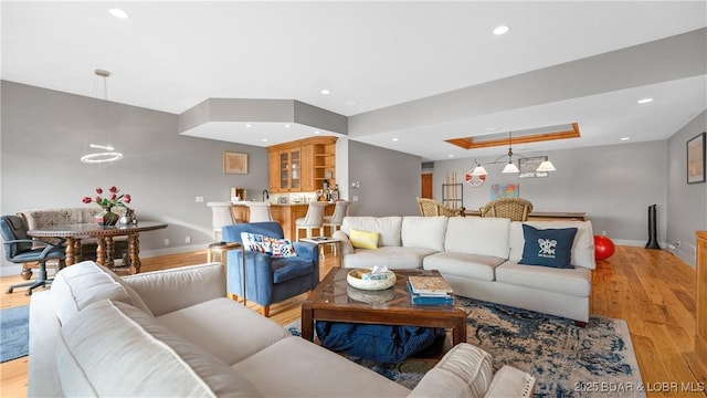 living room featuring recessed lighting, baseboards, a tray ceiling, and light wood-style floors