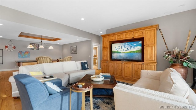 living room with recessed lighting, light wood-style flooring, a raised ceiling, and baseboards