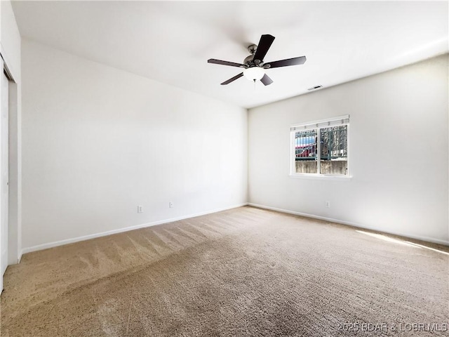 carpeted spare room with visible vents, baseboards, and ceiling fan