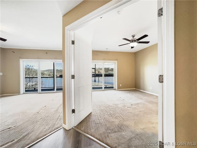 carpeted empty room featuring a ceiling fan, baseboards, and a water view