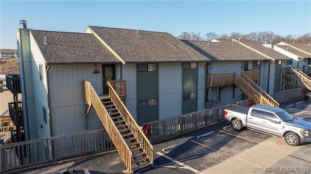 rear view of house with uncovered parking, stairs, and a shingled roof