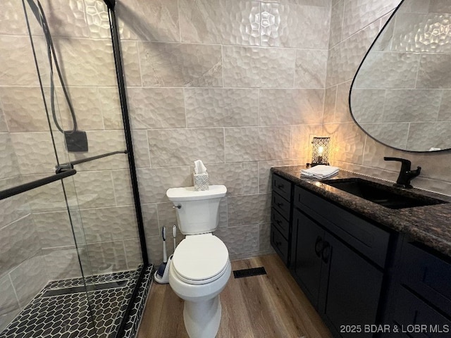 full bath with tile walls, toilet, a stall shower, wood finished floors, and vanity