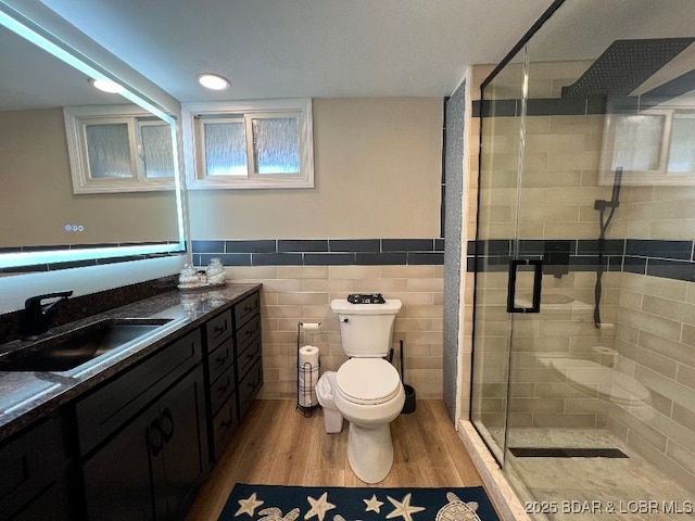 bathroom featuring tile walls, toilet, a stall shower, wood finished floors, and vanity