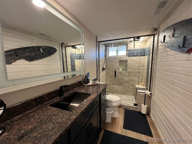 bathroom with vanity, wooden walls, visible vents, a shower stall, and toilet