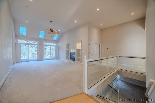 living room featuring baseboards, carpet floors, a skylight, a towering ceiling, and a ceiling fan