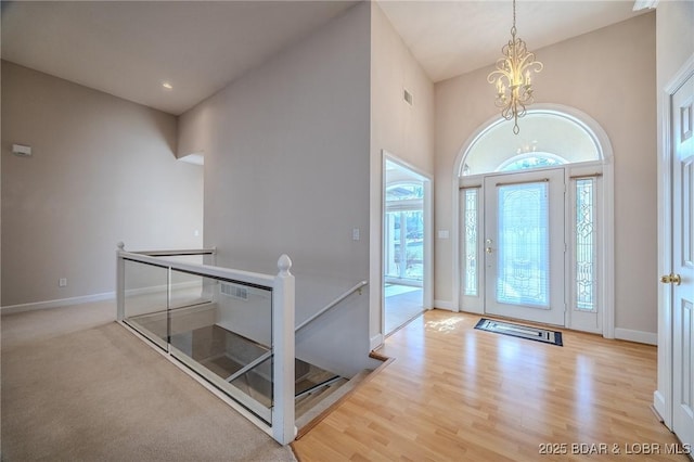 foyer with visible vents, wood finished floors, an inviting chandelier, baseboards, and a towering ceiling