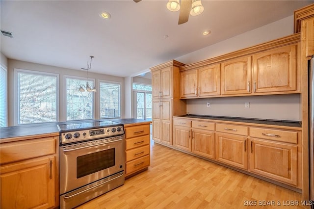 kitchen featuring electric range, light wood-style flooring, light brown cabinetry, dark countertops, and ceiling fan with notable chandelier