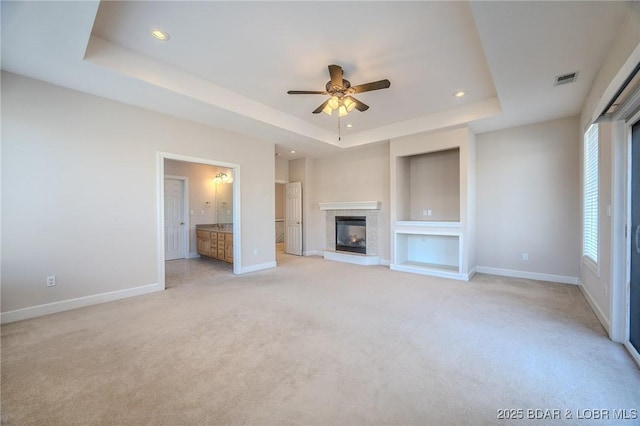 unfurnished living room with light carpet, baseboards, a tray ceiling, and a ceiling fan