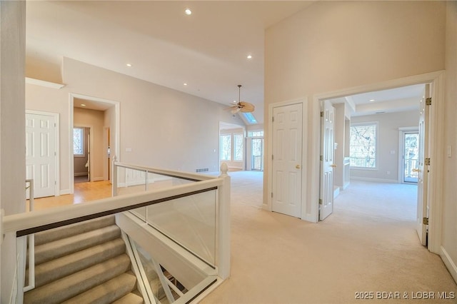 corridor featuring visible vents, baseboards, light carpet, recessed lighting, and a towering ceiling