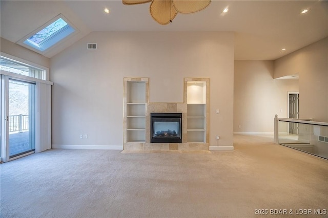 unfurnished living room featuring high vaulted ceiling, a skylight, carpet flooring, baseboards, and a tile fireplace