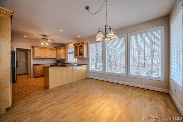 kitchen with glass insert cabinets, baseboards, light wood-style flooring, a peninsula, and freestanding refrigerator