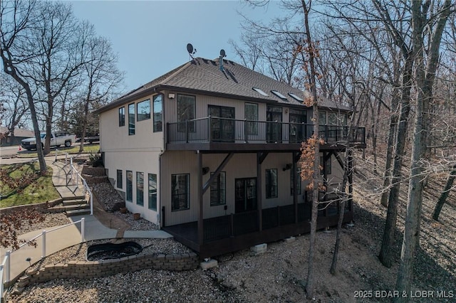 rear view of property featuring a wooden deck, a patio, and a shingled roof