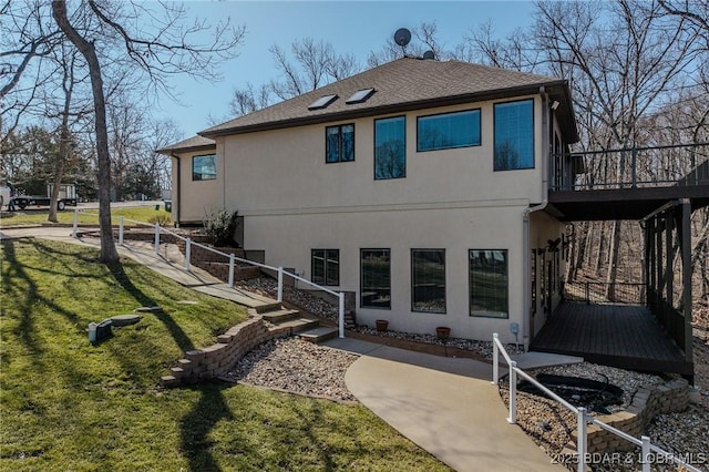 rear view of house featuring a shingled roof, a lawn, and stucco siding