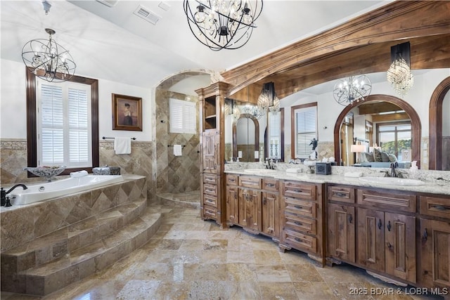 full bath featuring a bath, double vanity, a sink, walk in shower, and a notable chandelier