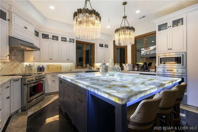 kitchen with a kitchen island, decorative backsplash, under cabinet range hood, appliances with stainless steel finishes, and a chandelier