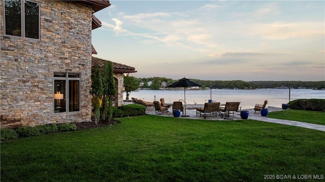 yard at dusk featuring a patio and a water view