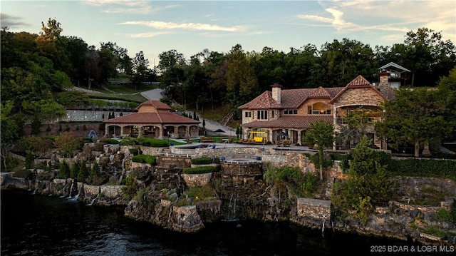 exterior space featuring a water view, stone siding, a gazebo, a chimney, and a tiled roof