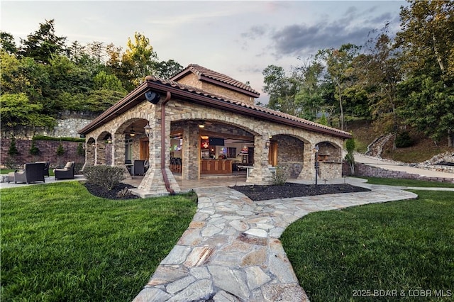 exterior space featuring a patio area, a tiled roof, a lawn, and stone siding