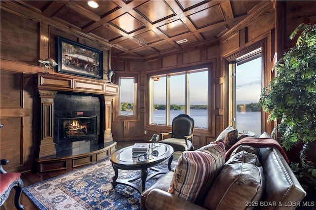 living area featuring a water view, wood walls, a premium fireplace, a decorative wall, and coffered ceiling