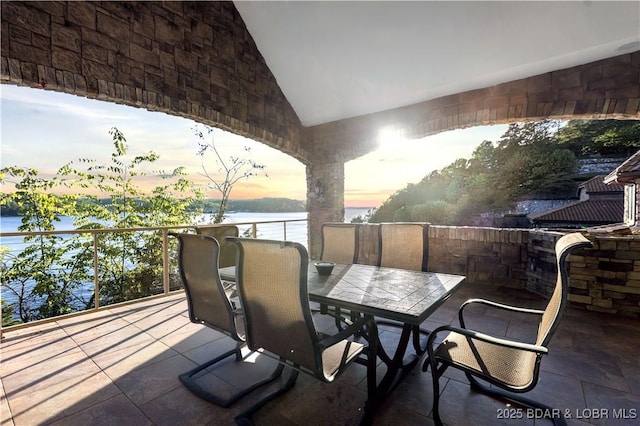 patio terrace at dusk featuring a water view, outdoor dining area, and a balcony