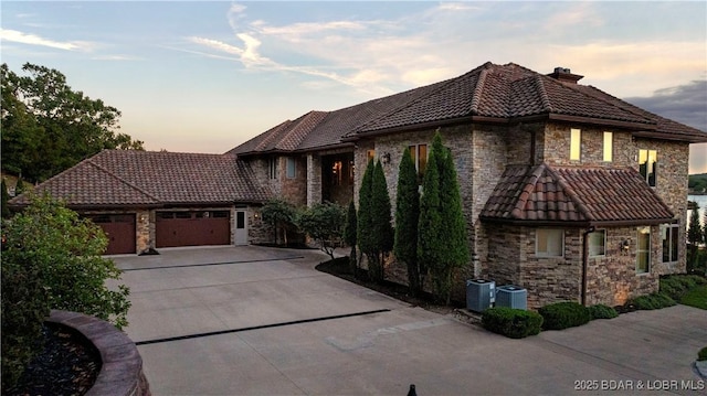view of front of house with a tiled roof, a chimney, a garage, concrete driveway, and stone siding