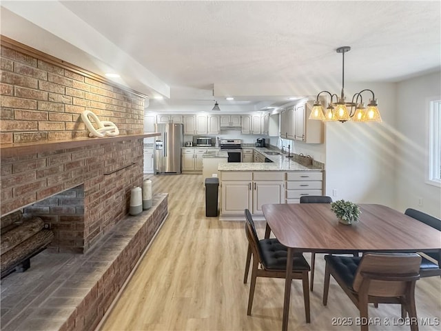 dining space with a brick fireplace, a notable chandelier, and light wood-type flooring