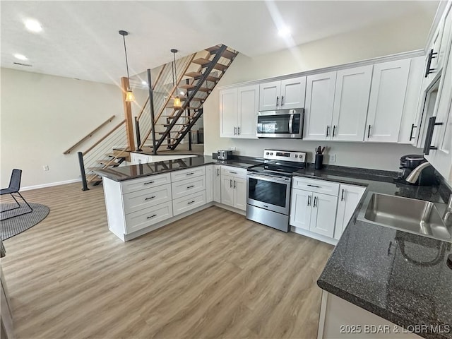 kitchen with appliances with stainless steel finishes, white cabinetry, a sink, a peninsula, and light wood-style flooring