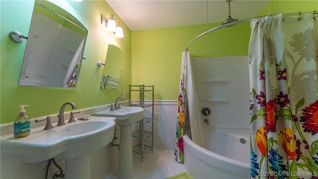 full bathroom with tile walls, shower / bathtub combination with curtain, a wainscoted wall, and a sink