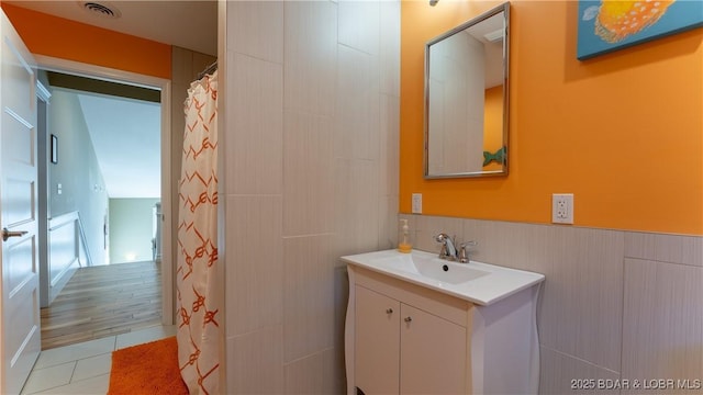 full bath featuring vanity, a wainscoted wall, visible vents, and tile patterned floors