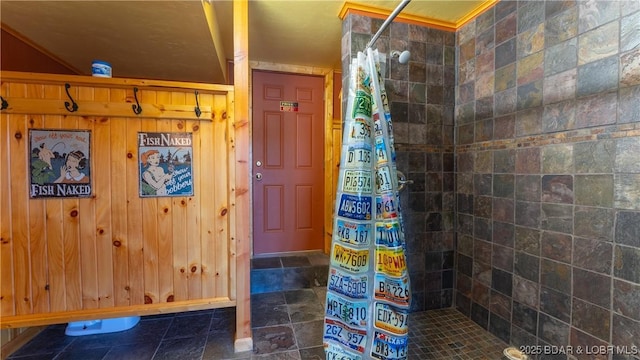 full bath featuring tiled shower and wood walls