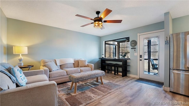 living room featuring a textured ceiling, wood finished floors, baseboards, and ceiling fan