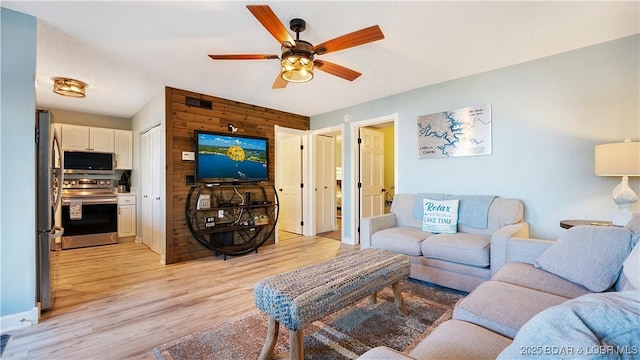 living area with baseboards, wood walls, a ceiling fan, and light wood finished floors