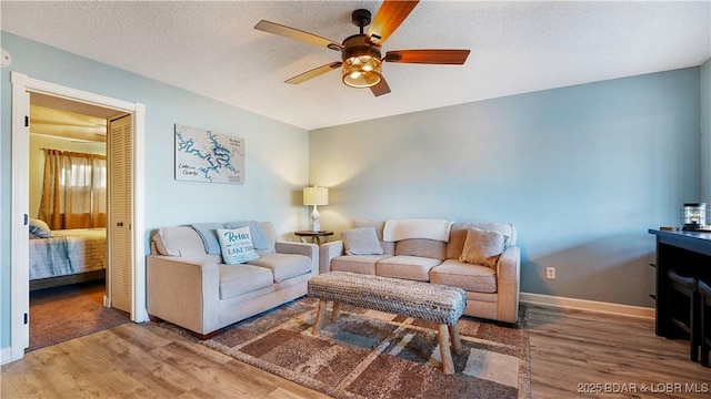 living area featuring baseboards, a textured ceiling, wood finished floors, and a ceiling fan