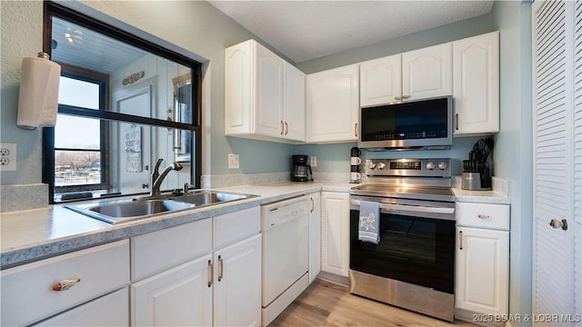 kitchen with light wood-type flooring, light countertops, stainless steel appliances, white cabinetry, and a sink