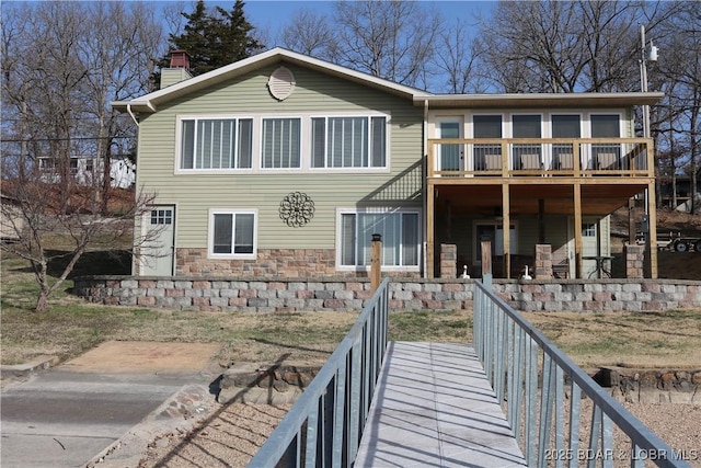 back of house with stone siding, a deck, and a chimney