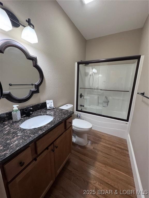 full bath featuring baseboards, toilet, wood finished floors, enclosed tub / shower combo, and vanity