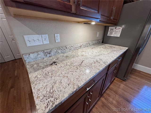 kitchen with baseboards, light stone countertops, dark wood-style flooring, and freestanding refrigerator