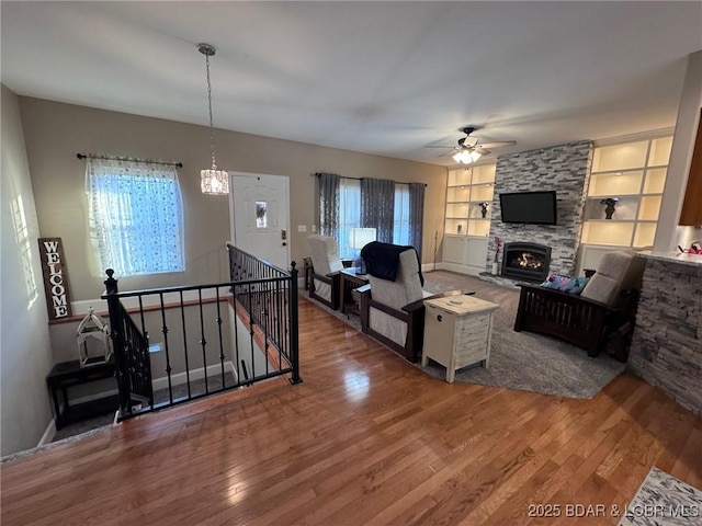 living area featuring built in shelves, a ceiling fan, baseboards, a fireplace, and wood-type flooring