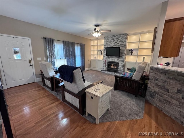 living room with a wealth of natural light, a stone fireplace, a ceiling fan, and wood finished floors