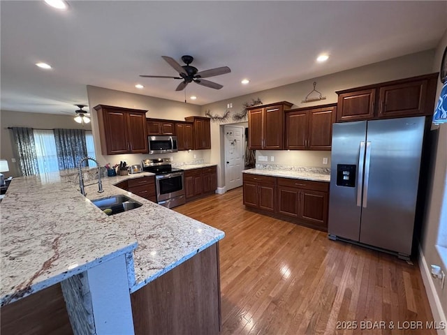 kitchen featuring dark brown cabinetry, light wood-style floors, stainless steel appliances, a ceiling fan, and a sink