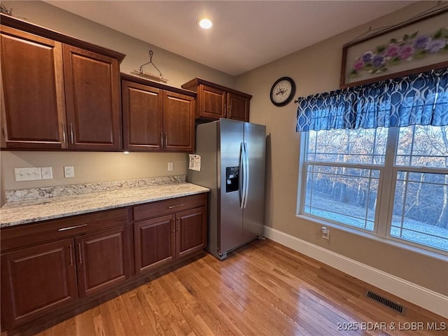 kitchen with light stone counters, visible vents, light wood finished floors, baseboards, and stainless steel fridge