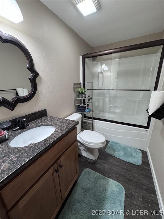 full bath featuring baseboards, toilet, wood finished floors, combined bath / shower with glass door, and vanity